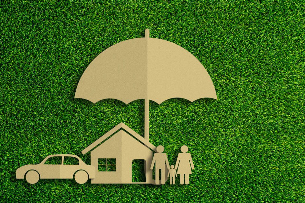A family with a house and a car underneath an umbrella made out of cardboard, laid on top of grass