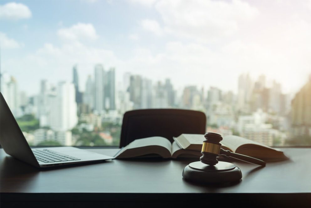 A gavel on a table with a computer and a book and the skyline of a city in the background